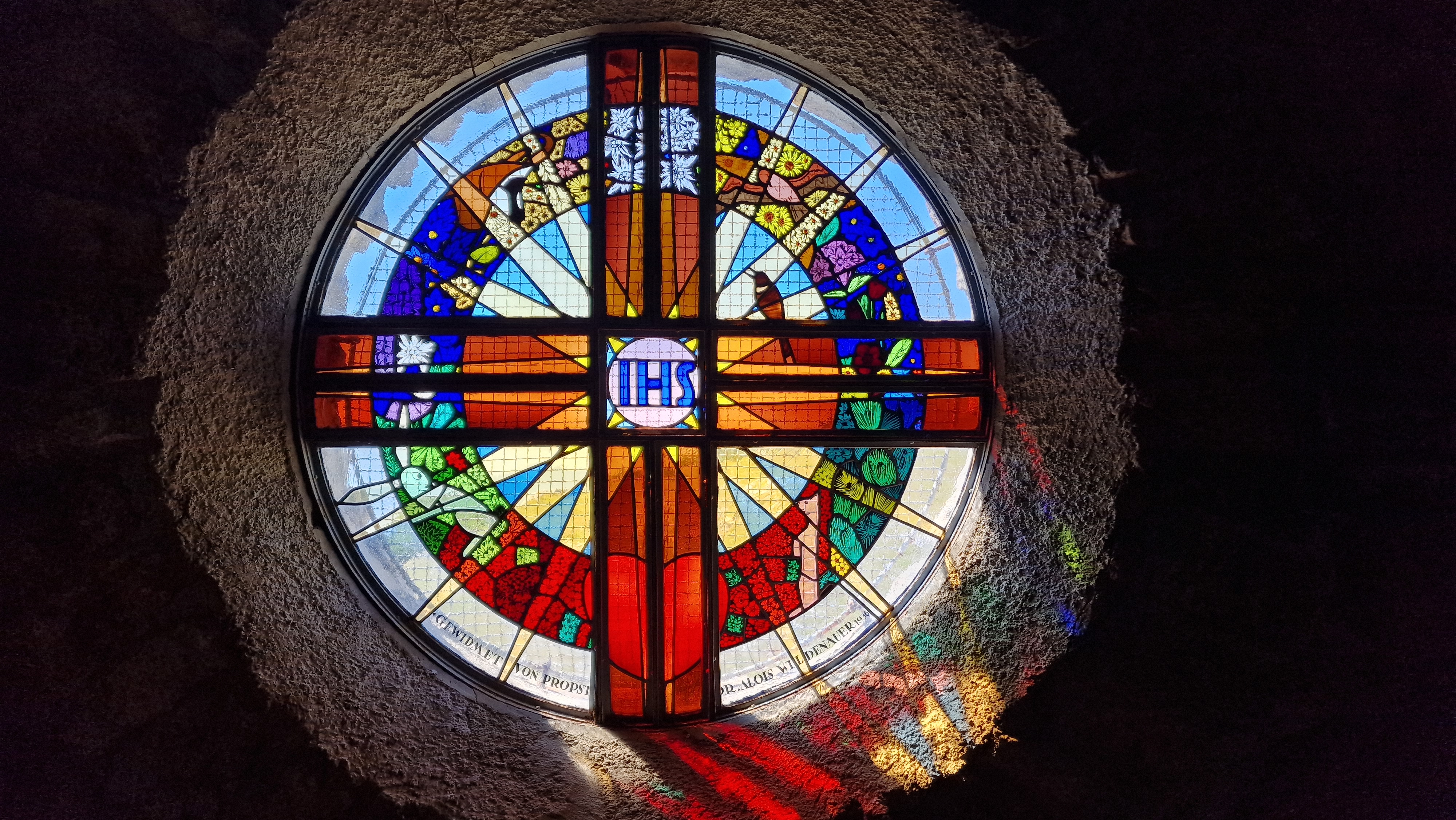 Foto von dem runden bunten Fenster der Raxkirche